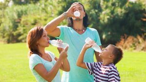 Stay Hydrated - Family with a woman, a man, and a child drink water out of water bottles outside. Community Health Centers of South Central Texas
