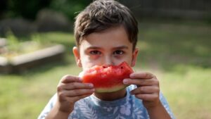 Blog post image - Stay Hydrated - Boy holds up a watermelon slice in front of his face.