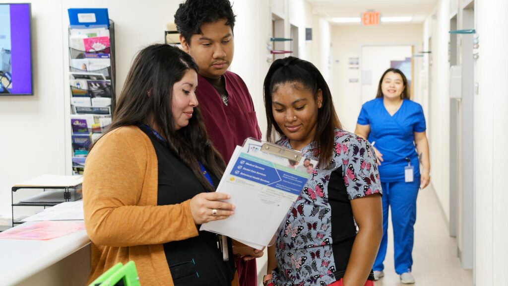 Three health center employees discuss a patient's chart.