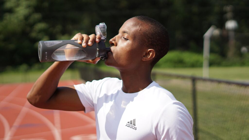 Stay hydrated - man drinks water from a water bottle while on a track. The importance of hydration. Community Health Centers of South Central Texas