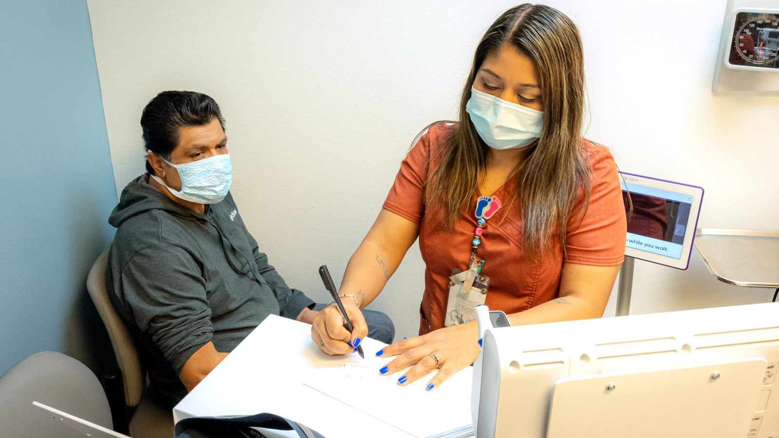 Male patient sits in an exam room with a female nurse for a sick visit at Community Health Centers of South Central Texas for annual exams and sick visits VISITAS POR ENFERMEDAD